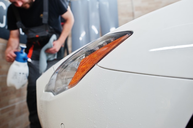 O trabalhador no detalhamento da garagem colocou uma capa de filme anti-cascalho de poliuretano em um carro branco de luxo.