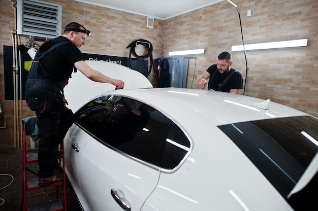 O trabalhador no detalhamento da garagem colocou uma capa de filme anti-cascalho de poliuretano em um carro branco de luxo.