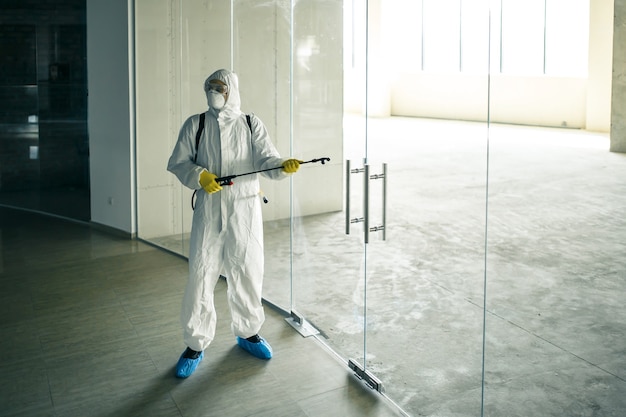 Foto o trabalhador sanitário borrifa um centro de negócios vazio com um líquido anti-séptico para evitar que o covid-19 se espalhe. um homem vestindo roupa de desinfecção, limpando o shopping. ninguém, saúde, conceito isolado.