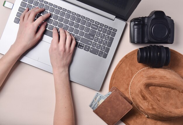 Foto o trabalho do fotógrafo, retoque de fotos. equipamento fotográfico, chapéu, carteira, mãos femininas, digitando no teclado do laptop em fundo pastel, vista superior, conceito de freelancing, configuração plana