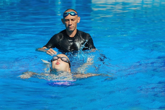 O treinador de natação conduz uma aula individual com a garota na piscina externa