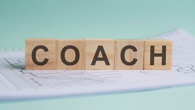 O treinador é escrito em blocos de madeira leves. a palavra está localizada em uma folha com tabelas e gráficos. conceito de negócios.