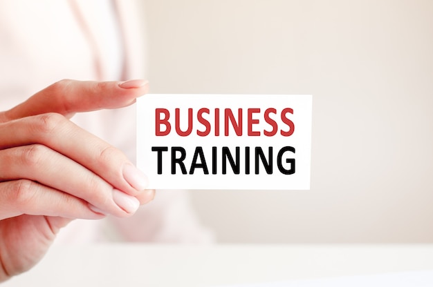 O treinamento empresarial é escrito em um cartão branco na mão de uma mulher. Fundo rosa.