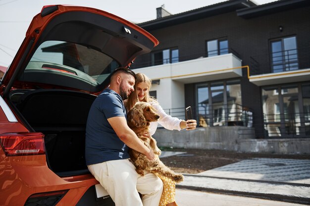 O tronco está aberto. Lindo casal passear com o cachorro ao ar livre perto do carro.