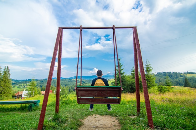 O turista de cara sentar no balanço e desfrutar da paisagem de natureza amzing das montanhas Karpaty de verão.