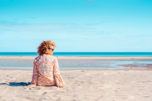 O turista de pessoas do sexo feminino relaxa a atividade de lazer sentado na areia na praia aproveitando o sol e a vista para o mar Céu claro e viagens férias férias conceito de mulher Copie o fundo do espaço