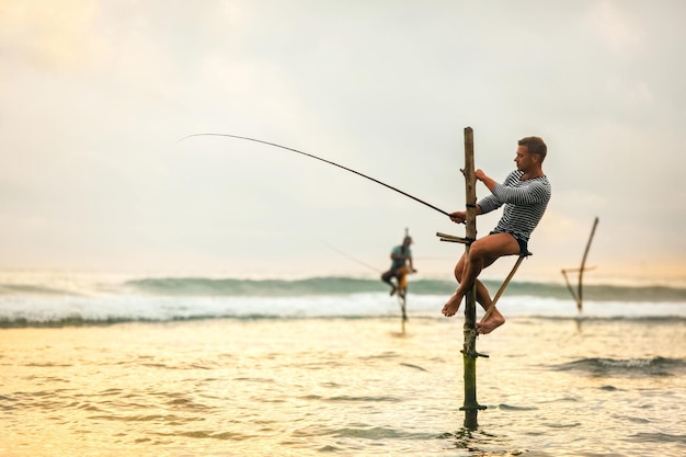 O turista europeu está envolvido na pesca tradicional em postes no Oceano Índico Sri Lanka