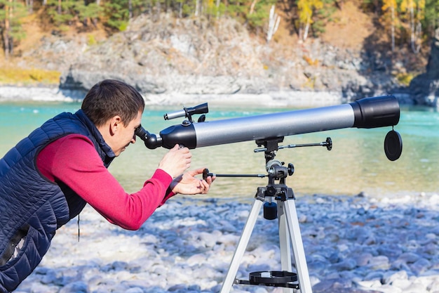 O turista olha na distância através do telescópio no fundo do rio da montanha nas montanhas
