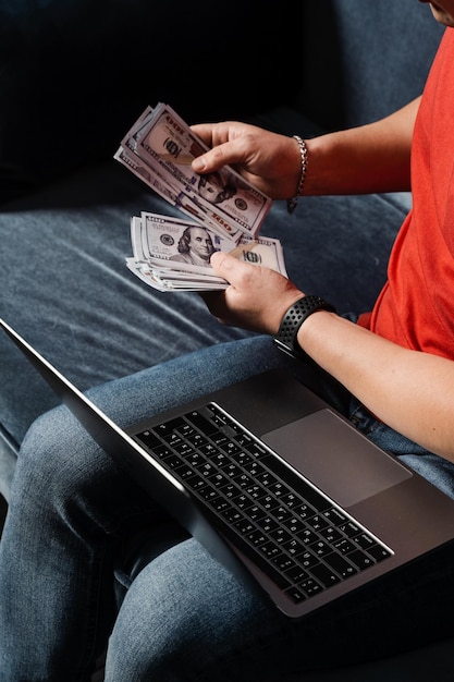 O vencedor no casino online está contando o dinheiro ganho O homem com laptop está contando dólares em dinheiro e ganha a aposta online