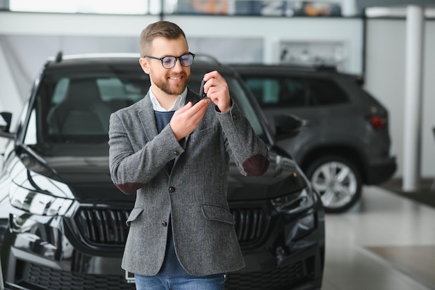 O vendedor alegre e amigável bonito posa em um salão de carro ou showroom