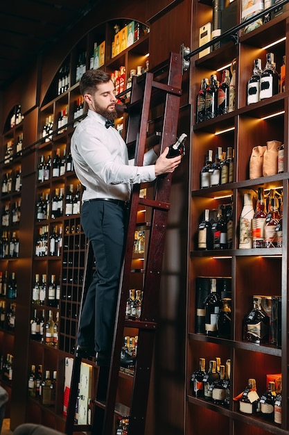 Foto o vendedor de bebidas alcoólicas classifica garrafas em pé na escada.