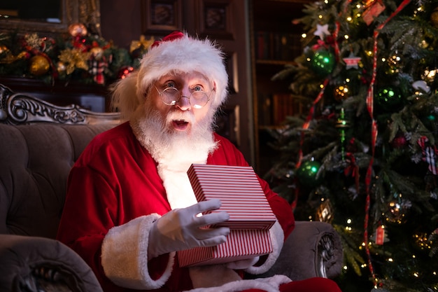 O verdadeiro autêntico papai noel surpreso com o presente de natal. realização de desejos. papai noel sentado em