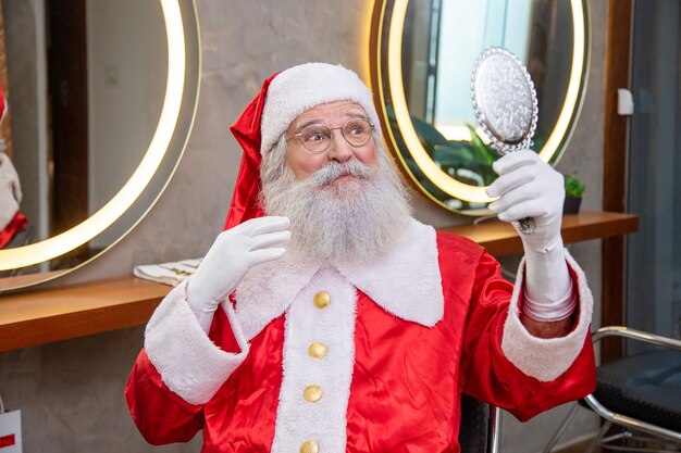 O verdadeiro Papai Noel na barbearia segurando um espelho, olhando para si mesmo.