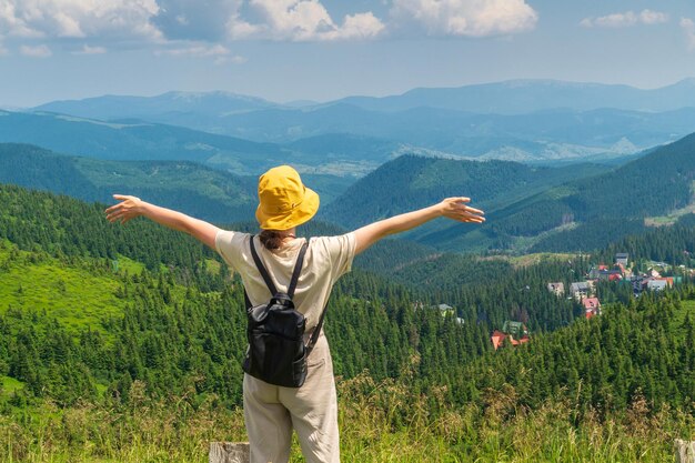 O viajante com uma mochila fica com os braços estendidos nas montanhas no verão