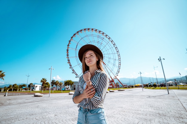 O viajante da mulher em um chapéu anda no porto na roda gigante na cidade de estância Batumi, Geórgia durante férias