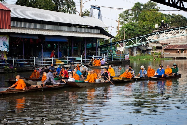 O viajante estrangeiro do povo tailandês visita e junta-se ao ritual de mérito da tradição e reza oferecendo esmolas dando à procissão do monge no barco no canal em Wat Sai Yai em 8 de novembro de 2022 em Nonthaburi, Tailândia
