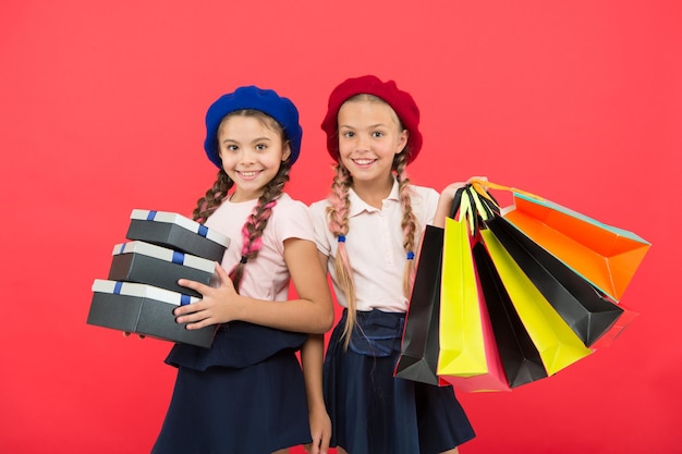 Foto obcecado por shoppings e shoppings de roupas conceito de viciado em compras as compras tornam-se divertidas com os melhores amigos crianças estudantes fofas seguram sacolas de compras crianças satisfeitas com compras de fundo vermelho