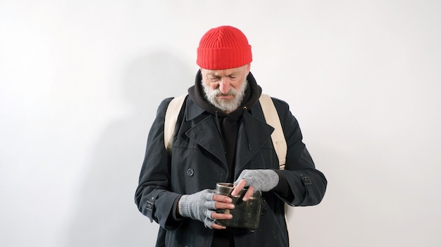 Obdachloser, ein Rentner, ein alter Mann mit einem grauen Bart in einem Mantel und einem roten Hut auf einem isolierten weißen Hintergrund