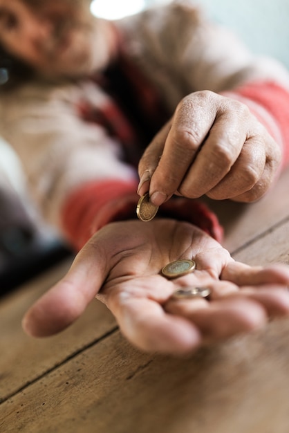 Obdachloser in zerrissenem Pullover, der seine letzten Euro-Münzen zählt. Konzentrieren Sie sich mit Münzen auf seine Handfläche.