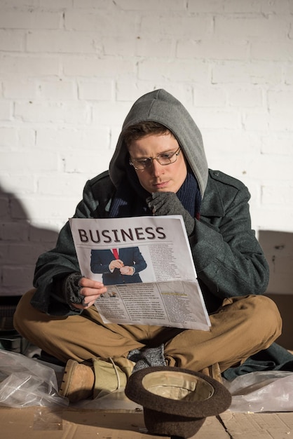 Obdachloser mit Brille liest aufmerksam Wirtschaftszeitung