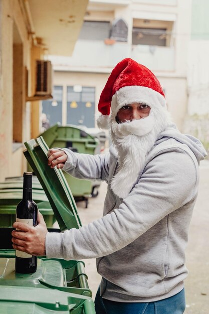 Obdachloser Weihnachtsmann, der Wein trinkt und Mülltonnen durchwühlt.