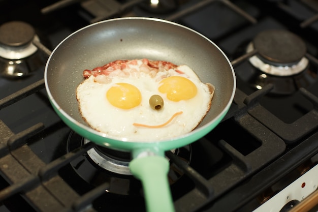 Oben Ansicht Nahaufnahme von Spiegeleiern in der Pfanne auf Gasherd mit lustigem Gesicht, Kinderessen und Frühstückskonzept, Kopienraum