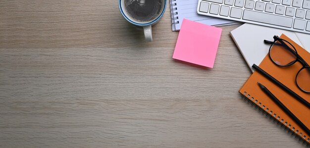 Oben Ansicht Schreibtisch mit Haftnotiz, Kaffeetasse, Tastatur und Notebook auf Holztisch.