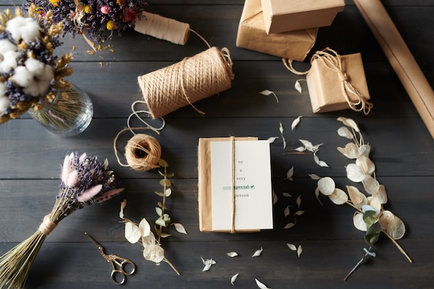 Oben Ansicht von verpackten Geschenken auf Tisch mit unordentlichen Blütenblättern, Schere, Schnur, Stapel von Geschenkboxen und getrockneten Blumen