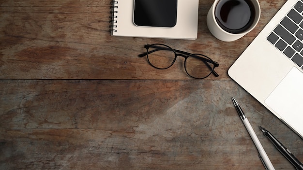 Oben Blick auf Computer-Laptop, Kaffeetasse, Smartphone, Brille und Notebook auf Holztisch.