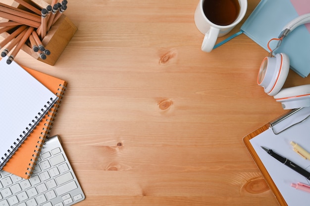 Oben Blick auf den Designer-Arbeitsplatz mit Kopfhörer, Bleistifthalter, Kaffeetasse und Notizbuch auf Holzschreibtisch.