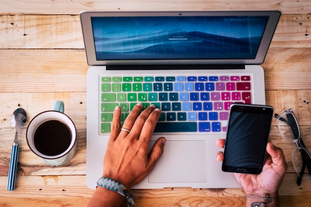 Oben Blick auf den Desktop-Arbeitsplatz mit Frauenhänden, die das Telefon mit dem Laptop verbinden, um einen modernen, intelligenten Online-Arbeitsjob zu starten - Konzept der Menschen, die mit Technologie am Schreibtisch arbeiten