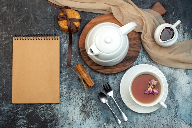 Oben Blick auf eine Tasse schwarzen Tee und Wasserkocher auf Holzbrett-Notebook-Keksen auf Eishintergrund