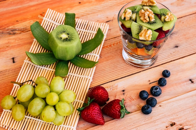 Oben Blick auf einen gemischten und frischen bunten Obstsalat in einer Glasschale. Frisches Obst im Hintergrund auf einem Holztisch