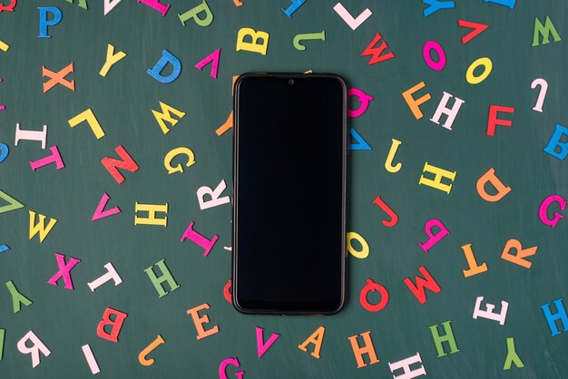 Oben oben Draufsichtfoto des Smartphones, das auf Greenboard mit bunten Buchstaben isoliert ist