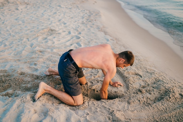 Oben ohne Mann am Strand, der Grube gräbt