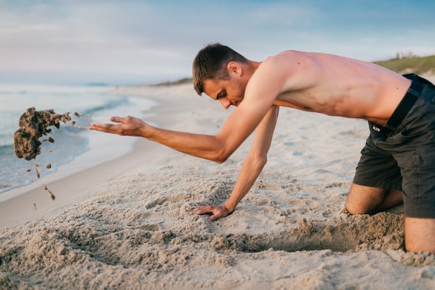 Oben ohne Mann am Strand, der Grube gräbt