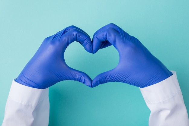 Oben über der Draufsicht Foto des Arztes in Handschuhen, der eine Herzform isoliert auf blaugrünem türkisfarbenem Hintergrund bildet