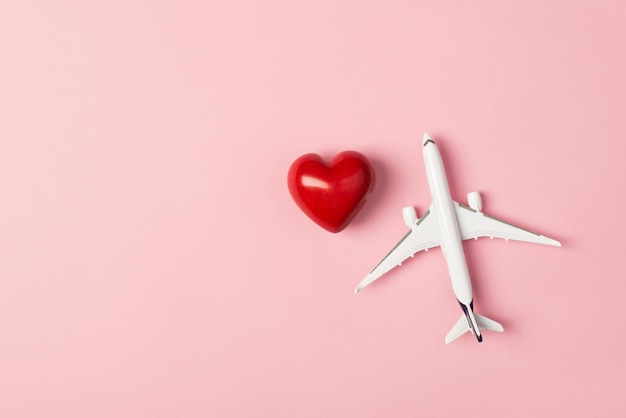 Obenliegendes Foto des Flugzeugs und des roten Herzens lokalisiert auf dem rosa Hintergrund mit Leerzeichen