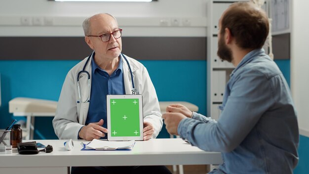 Oberarzt zeigt Greenscreen auf digitalem Tablet im Büro bei Kontrollbesuch. Gadget mit leerem Copyspace, Mockup-isolierter Vorlage und Chroma-Key-Hintergrund auf dem Display. Stativaufnahme.