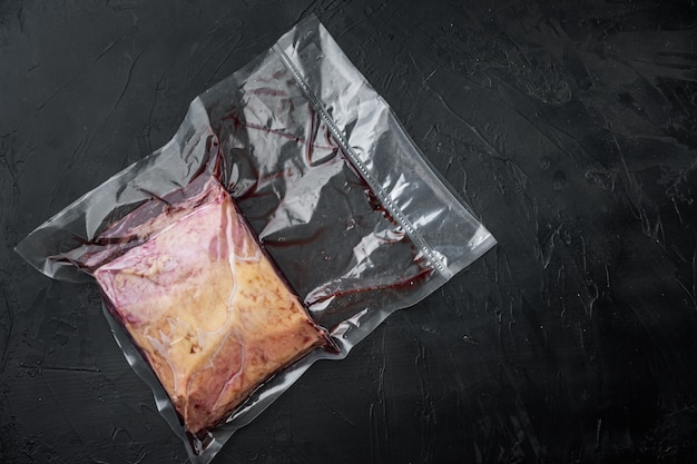 Oberes Lendenrindfleisch groß geschnitten in Plastikverpackung, auf schwarzem Tisch, Draufsicht,
