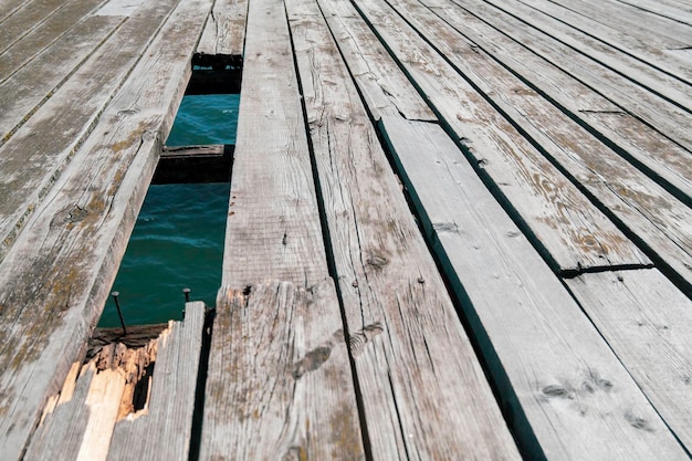 Oberfläche eines alten hölzernen Piers mit einem gebrochenen Brett und einem Loch im Boden mit Wasser des Meeres