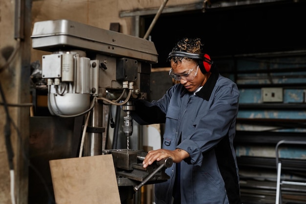 Oberkörperporträt einer Arbeiterin, die eine Maschineneinheit bedient und Metall in einer Industriewerkstatt bohrt