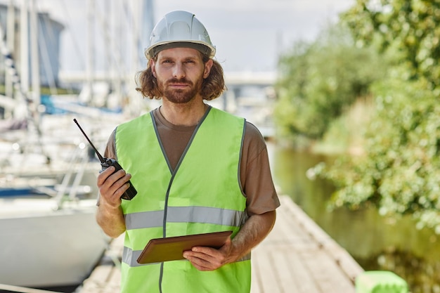 Oberkörperporträt eines jungen Mannes, der Radio hält und in die Kamera schaut, während er in einer Yachtdock-Kopie arbeitet