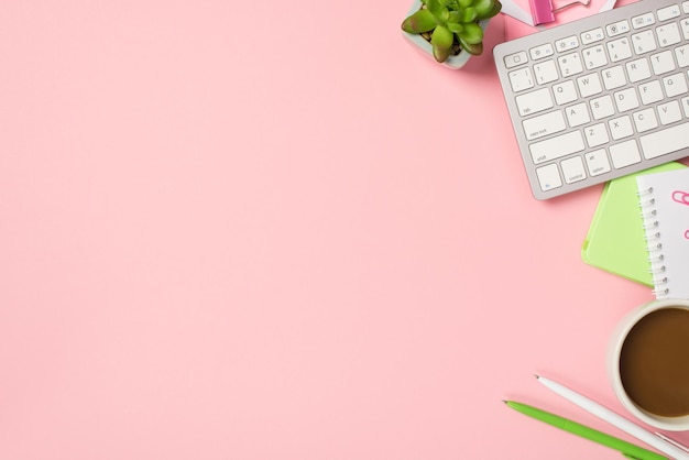 Obiges Foto der Tastatur Tasse Kaffee Notizblock Stifte Büroklammern und grüne Pflanze isoliert auf dem rosa Hintergrund mit Copyspace