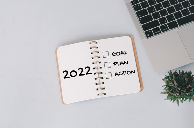 Objetivo de año nuevo 2022, plan, conceptos de acción con texto en el bloc de notas y computadora portátil en segundo plano.