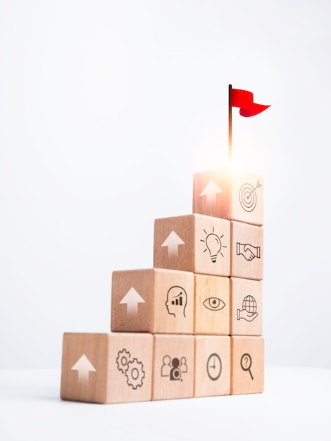 Objetivo de negócios com processo de sucesso de crescimento para o conceito de liderança. Bandeira vermelha no topo de blocos de cubo de madeira como um degrau com o ícone de estratégia de sinal de seta em fundo branco, estilo vertical.