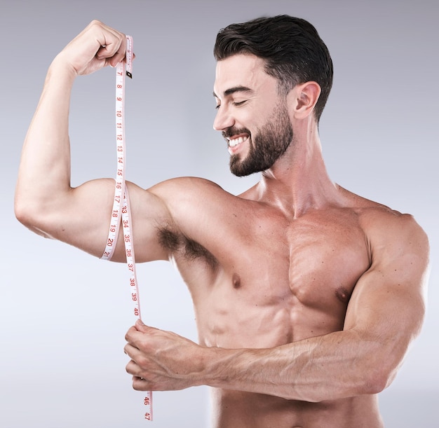 Objetivos de fitness ou homem forte com fita métrica para bíceps após exercício corporal no fundo do estúdio Fisiculturista feliz medindo braço para treino de treinamento ou resultados de progresso de crescimento muscular ou alvo