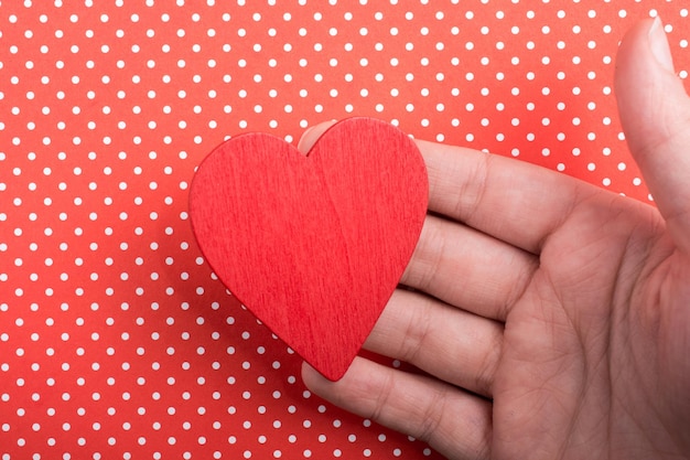 Objeto en forma de corazón de color rojo en la mano sobre papel punteado