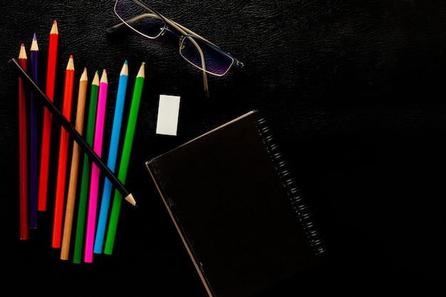 Objetos comerciales de lápices, papel y gafas sobre fondo de cuero negro