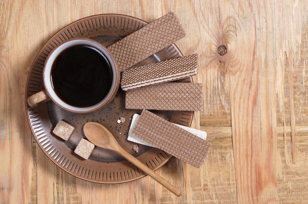 Obleas de chocolate y una taza de café caliente en un plato para desayunar sobre un fondo antiguo de madera, vista superior con espacio para copiar